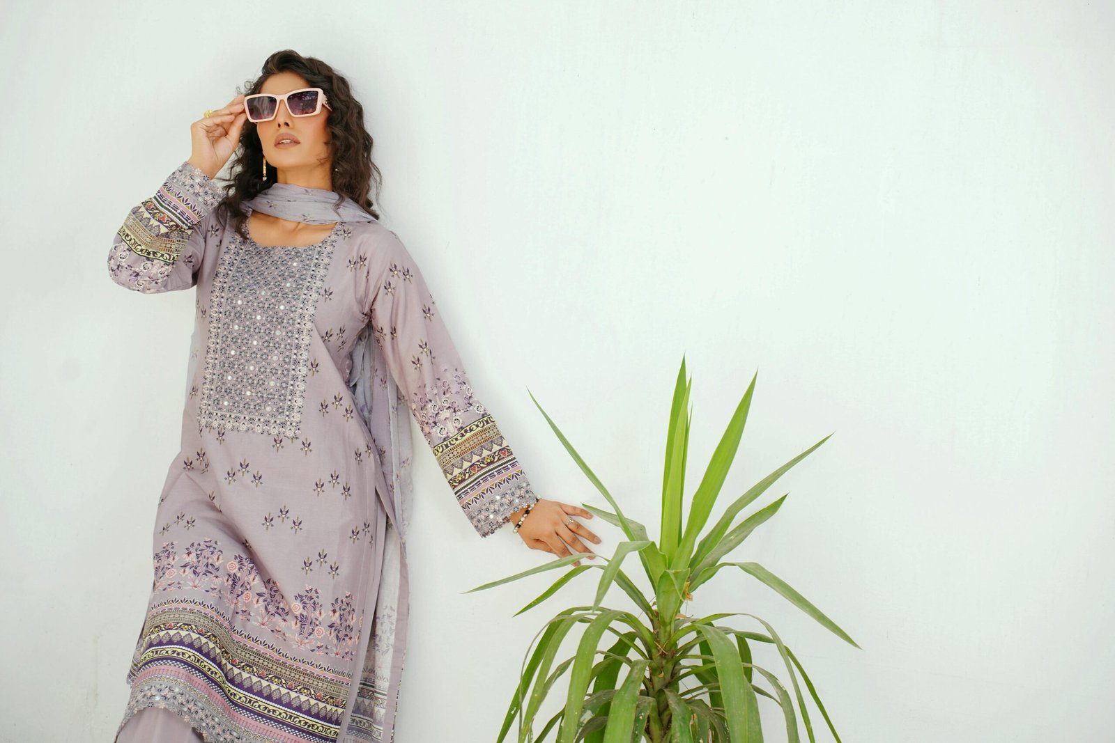 Home Elegant woman in traditional attire with sunglasses against a wall in Lahore, Pakistan.